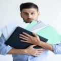puzzled-office-worker-holding-pile-documents (1)